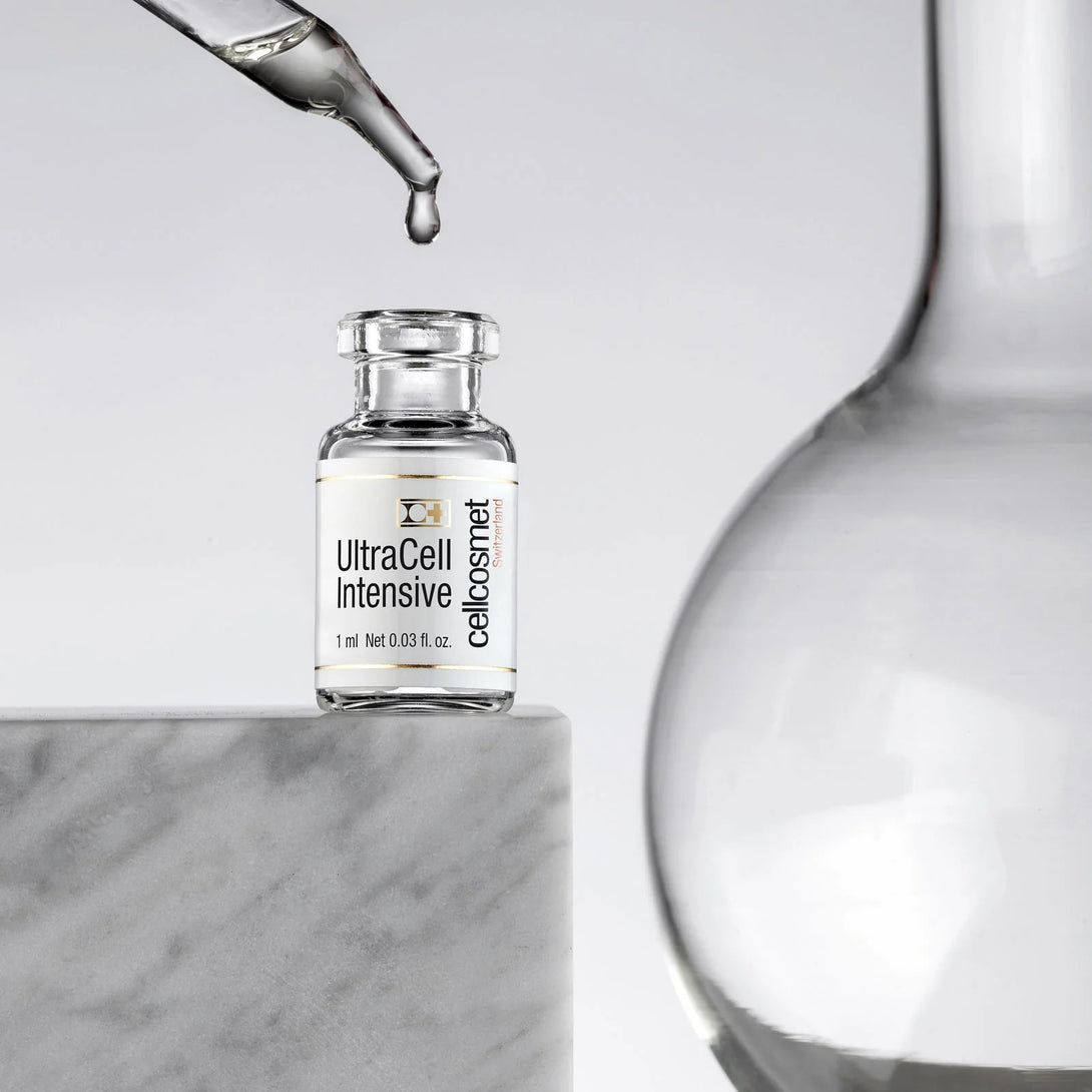 Glass bottle labeled 'UltraCell Intensive' with a dropper above it on a marble surface.