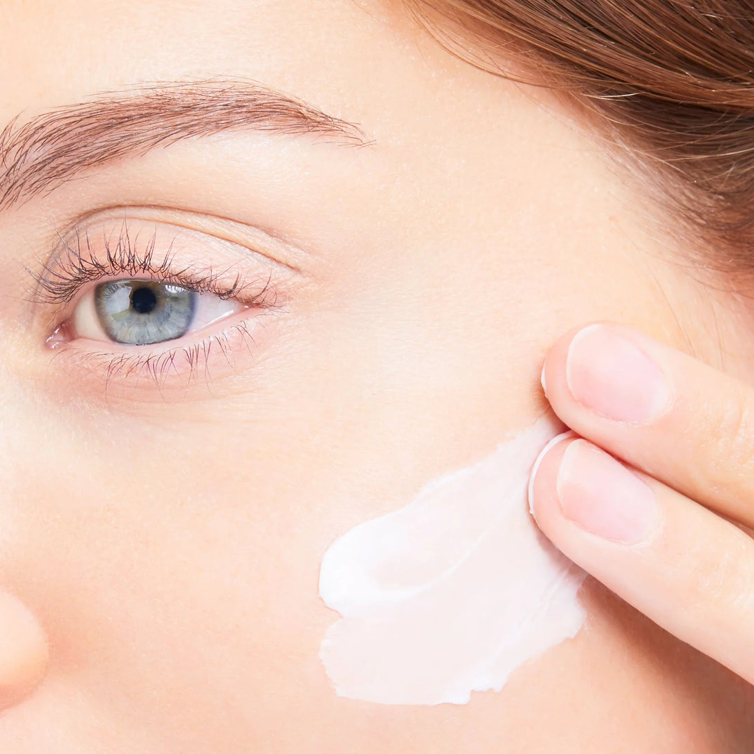 Close-up of a person applying cream to their face with a focus on the eye area.
