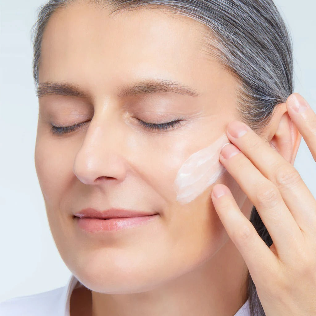 Woman applying cream to her face with a neutral background