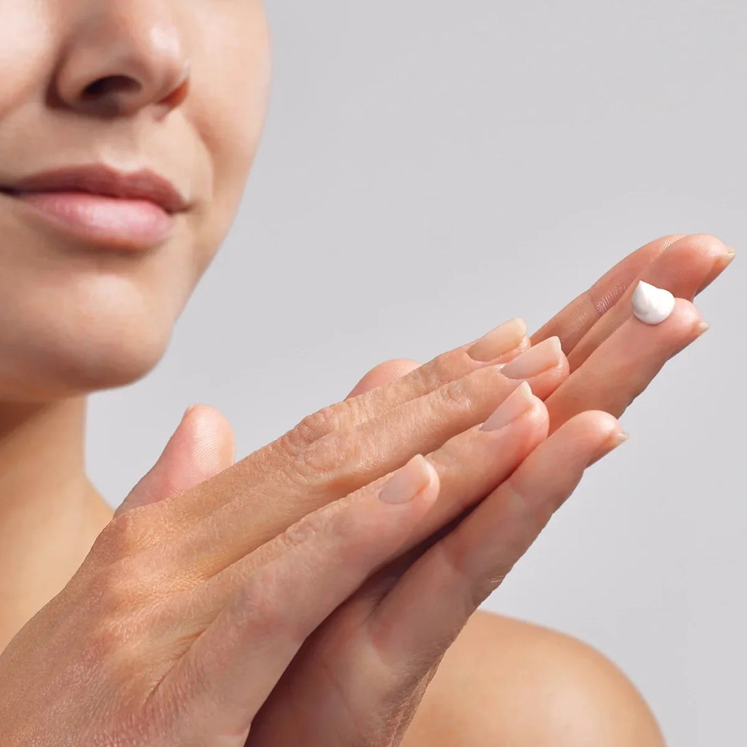 Close-up of a woman applying cream to her hand with a neutral background