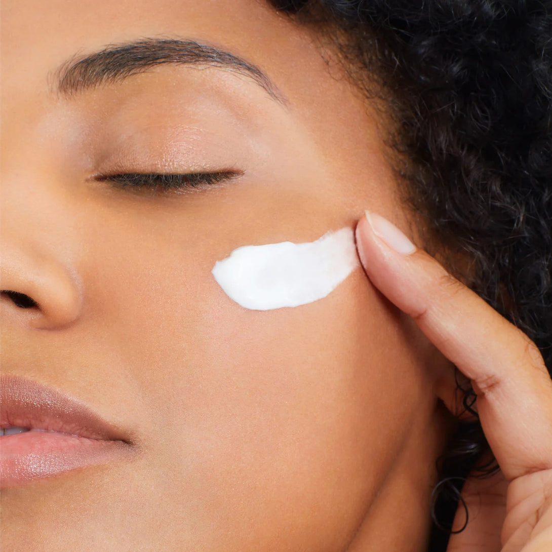 Close-up of a person applying white cream to their face.
