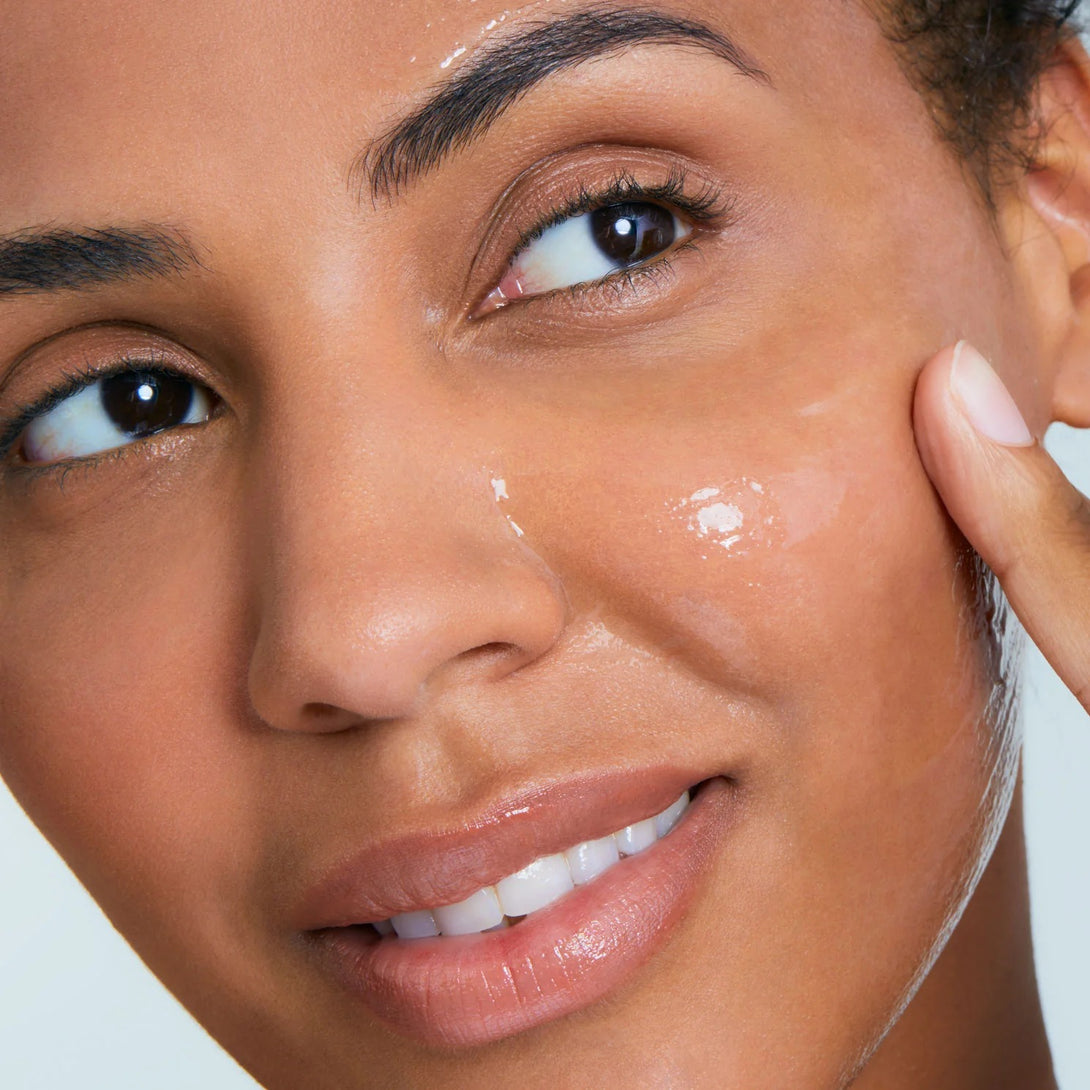 Woman applying skincare product to her face with a neutral background