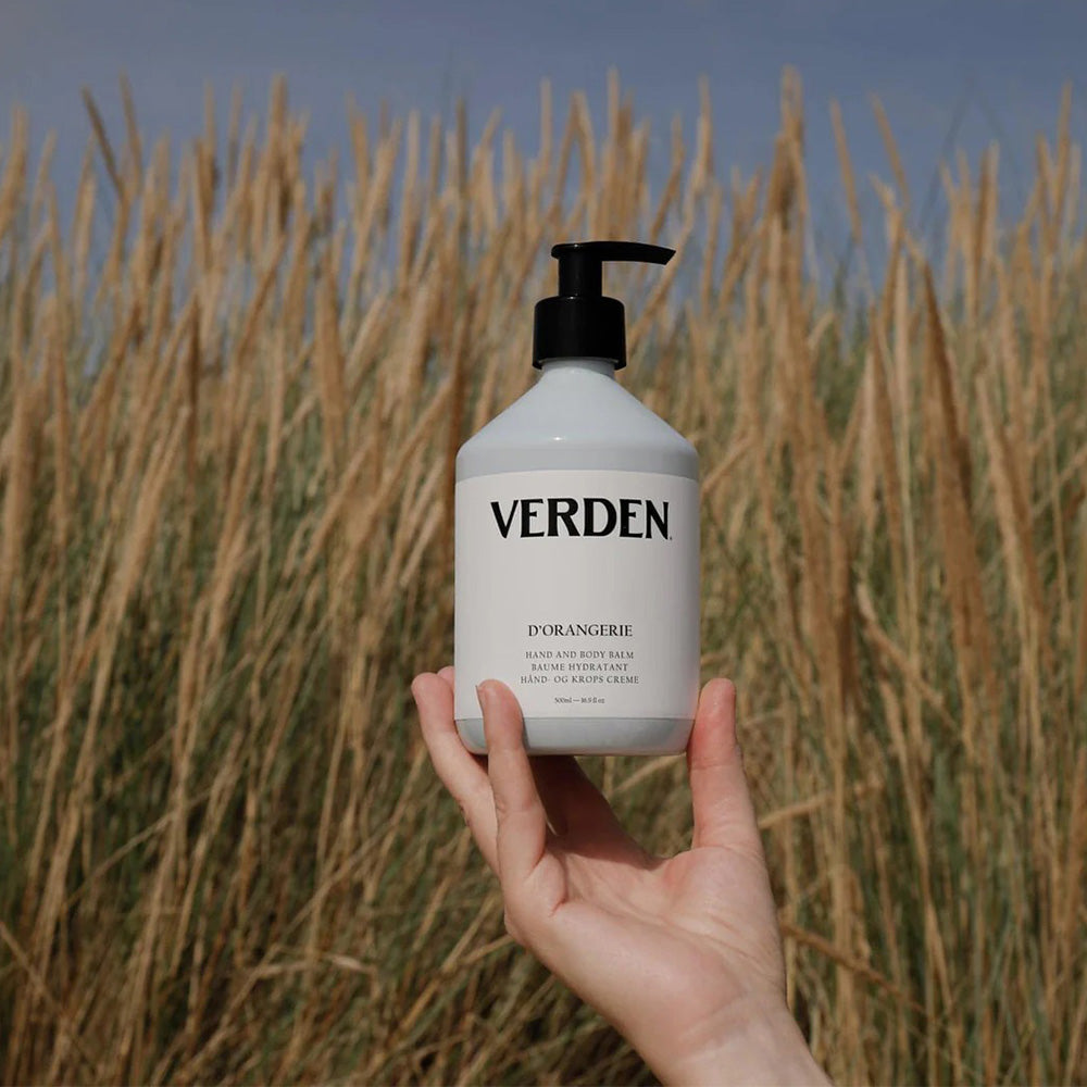 Hand holding a Verden bottle against a field of tall grass