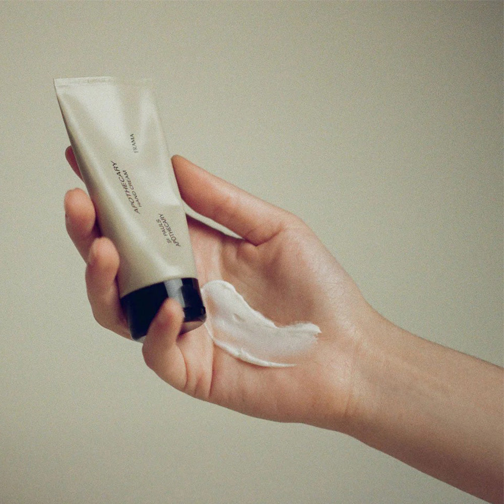 Hand holding a tube of cream with a small amount on the palm against a plain background